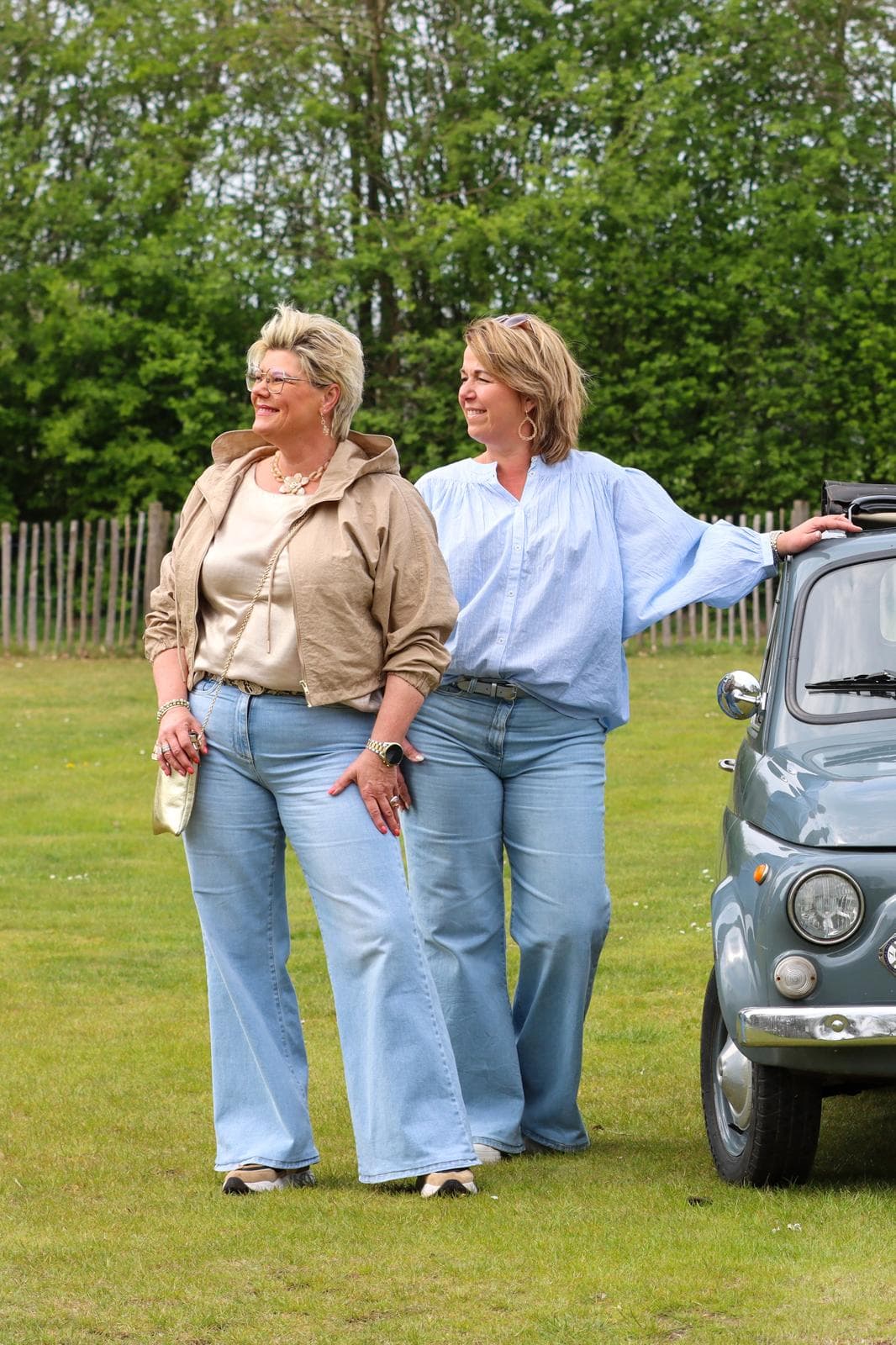 Eigenaressen van Label Trends in flared jeans naast een klassieke lichtblauwe Fiat 500 in de wei
