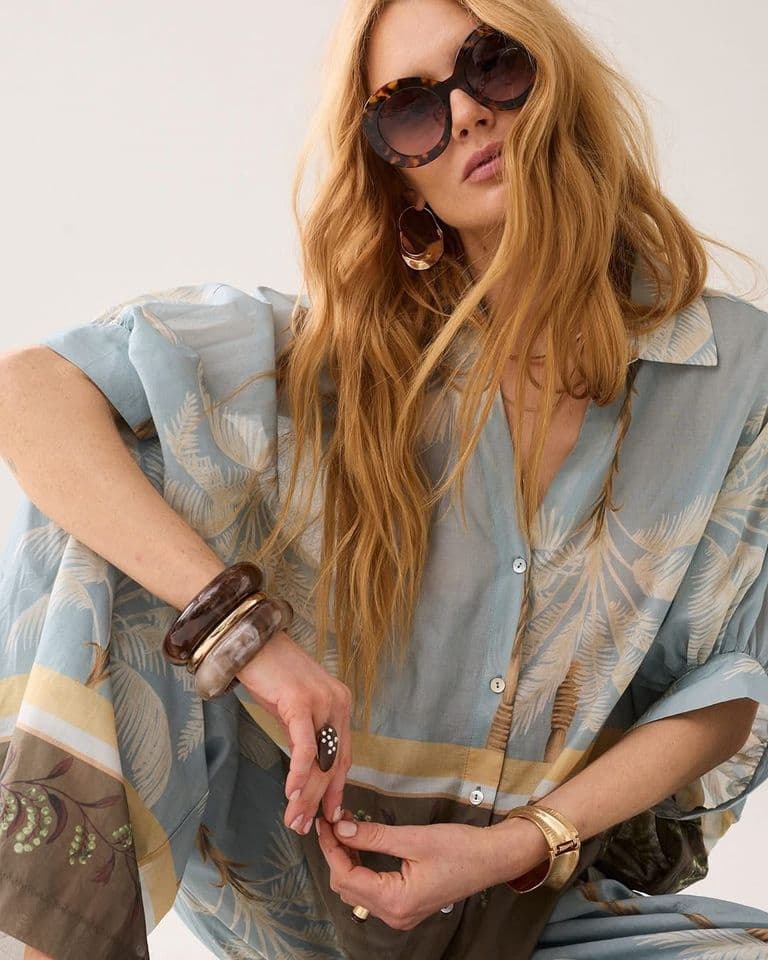Model met zonnebril in een lichtblauwe blouse met palmprint en armbanden, damesmode bij Label Trends