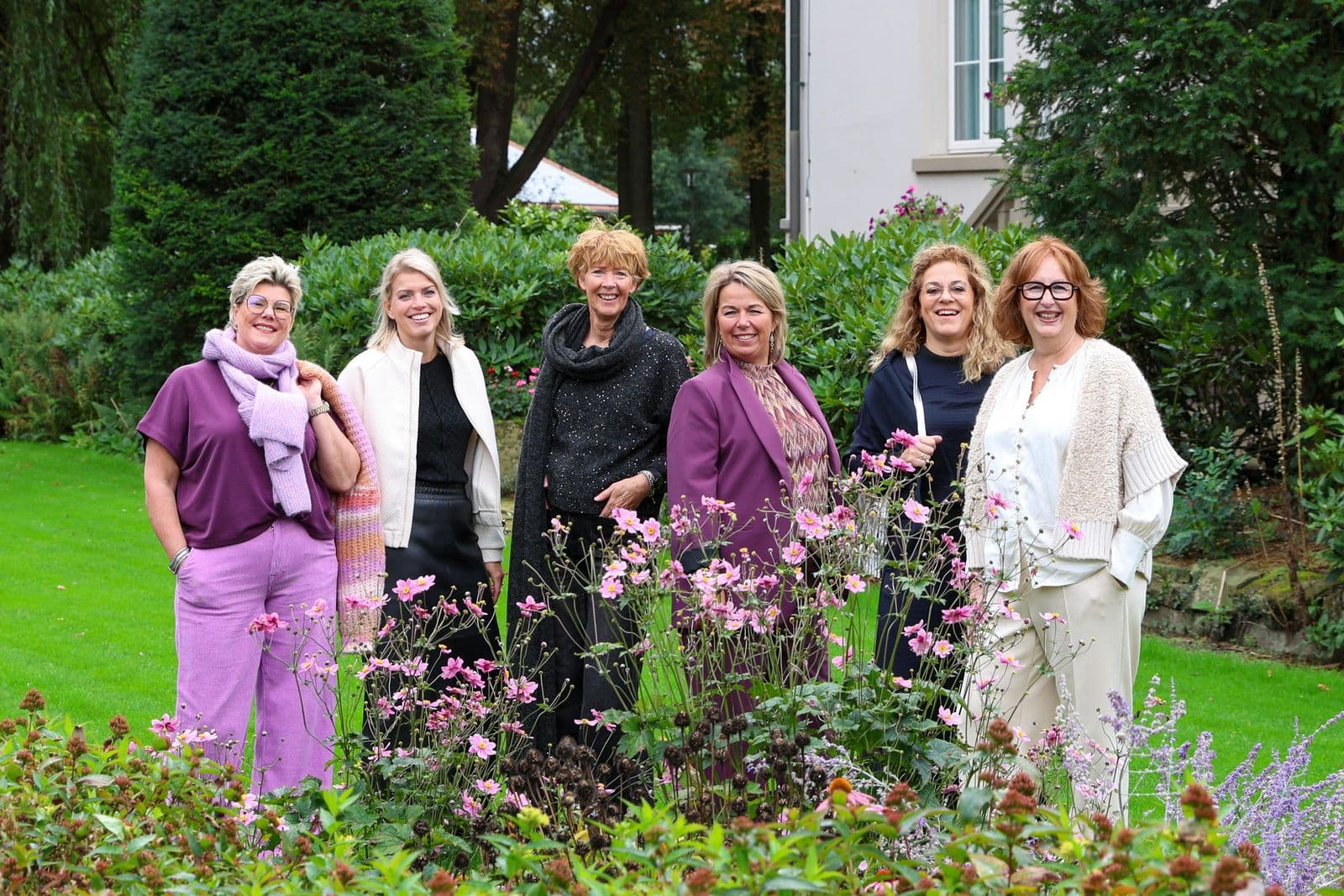 Het team van Label Trends in najaarslooks met paars en roze tussen de bloemen in de tuin